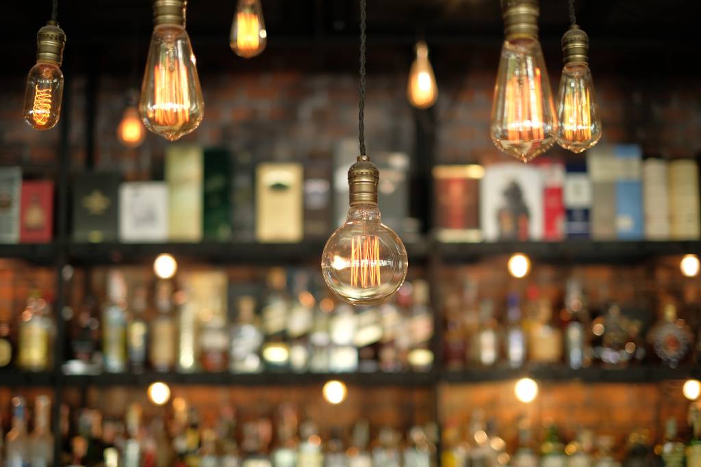 A photo of vintage lightbulbs over a nightclub bar with shelved liquor behind them.