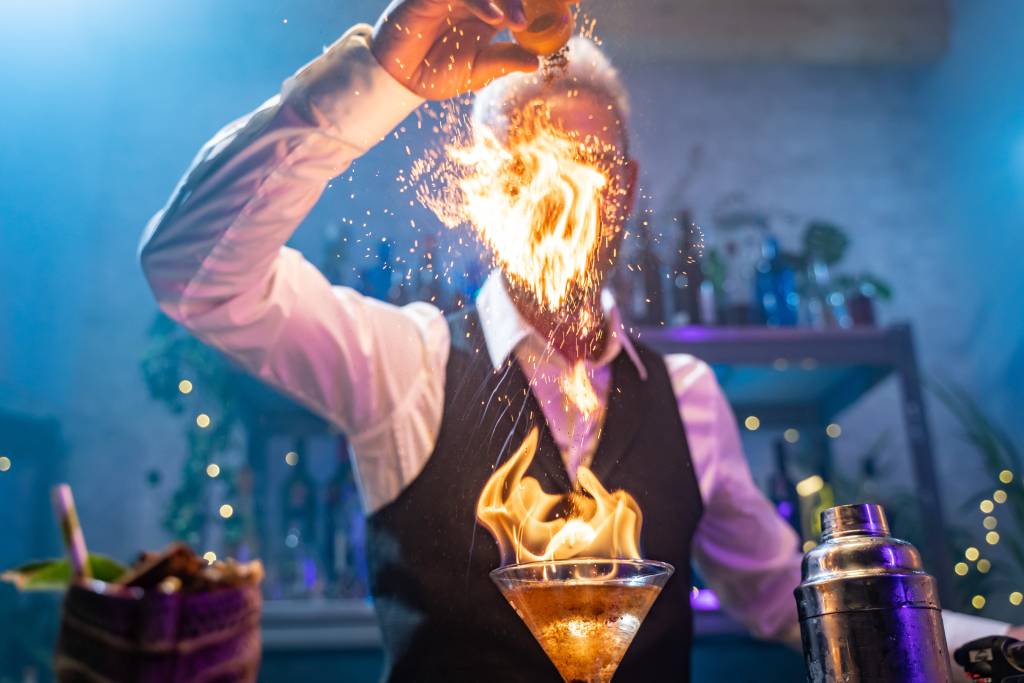 A nicely dressed bartender applying flame to a cocktail.