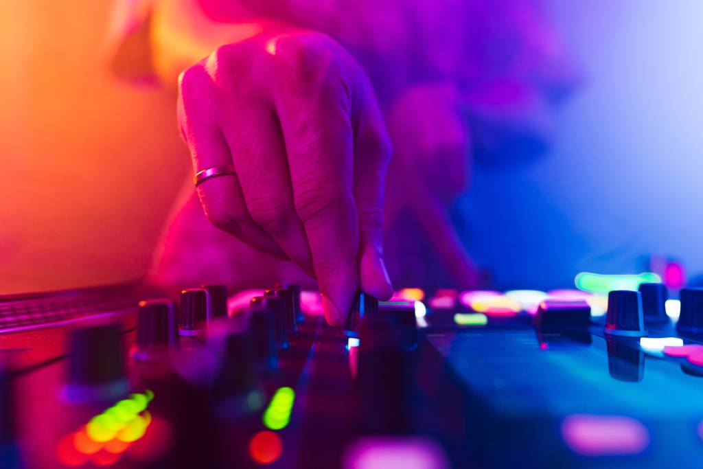 A close-up photo of a DJ’s hands mixing songs under colorful lights.