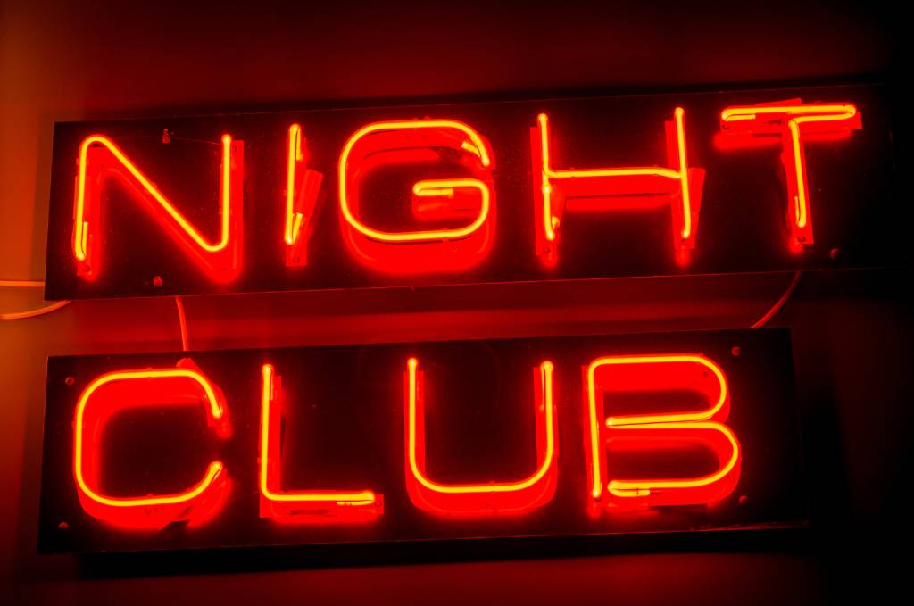 A red neon “night club” sign hanging on a wall.