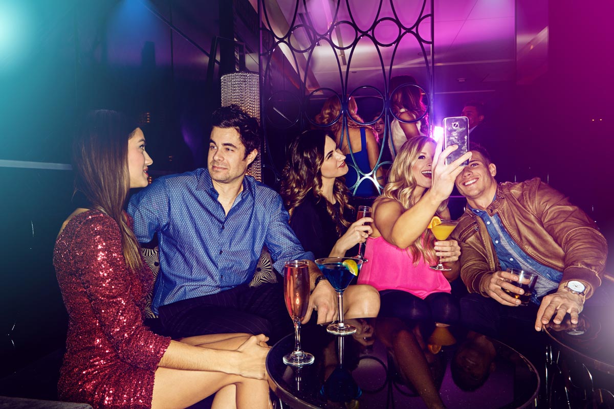 Five friends taking a selfie at a table in a nightclub.